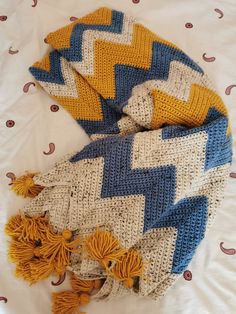 a crocheted blanket laying on top of a bed next to a yellow and blue scarf