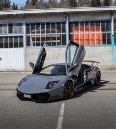 a grey sports car parked in front of a building with its doors open and the door opened