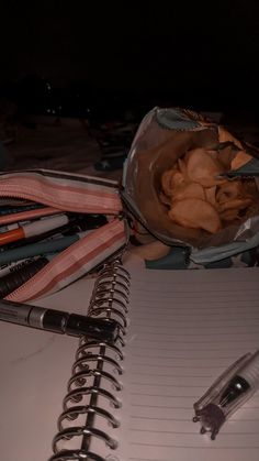 an open notebook with some pens and other items next to it on top of a table