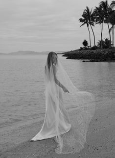 a woman in a wedding dress is standing on the beach with her veil over her head