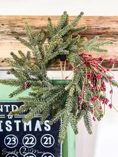 a christmas wreath hanging from the side of a green door with red berries on it