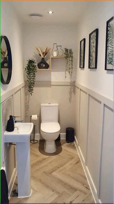 a white toilet sitting inside of a bathroom next to a sink and wooden flooring