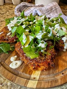 a wooden plate topped with meat patties covered in lettuce and sauces