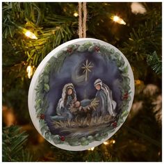 a christmas ornament hanging from a tree with nativity scene in the background