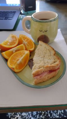 a sandwich and orange slices on a plate with a cup of coffee next to it