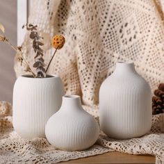 two white vases sitting on top of a table next to a lace doily