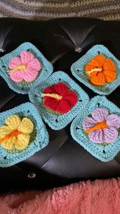 four crocheted flower coasters sitting on top of a black leather chair next to a pink blanket