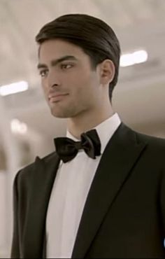 a man in a tuxedo and bow tie looks at the camera while standing