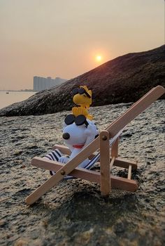 a stuffed animal sitting on top of a wooden chair in the sand near the ocean