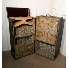 an old suitcase is open with a wooden hanger on it's side and another piece of furniture in the back