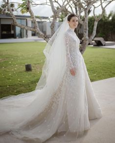 a woman wearing a wedding dress and veil standing in front of a tree with grass