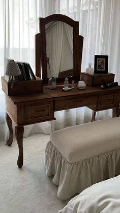 a wooden dressing table with a mirror and stool in front of a curtained window