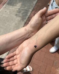 two people are holding hands with small tattoos on their arms and wrist, one has a tiny heart