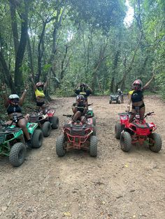 four people on four wheelers riding through the woods with their arms in the air