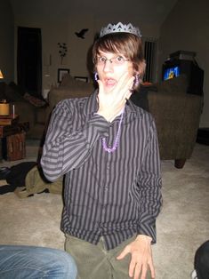 a man wearing a tiara making a silly face while sitting on the floor with his hands in his mouth