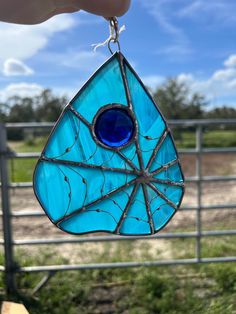 a hand holding a stained glass tear shaped ornament in front of a fence