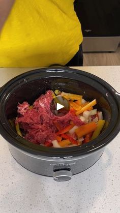 a crock pot filled with meat and vegetables on top of a white countertop