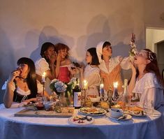 a group of women sitting around a table with food and candles