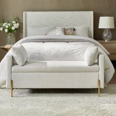 a white bed sitting in a bedroom next to a table with flowers on top of it