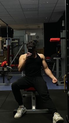 a man sitting on top of a bench in a gym holding a cell phone up to his face