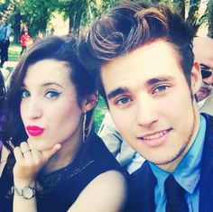 a man and woman posing for a photo in front of some people at an outdoor event