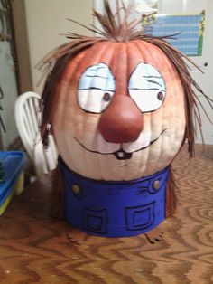 a large pumpkin shaped like a man with long hair and blue pants, sitting on top of a wooden table