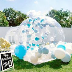 an inflatable bubble filled with blue and white balloons is on the grass next to a sign