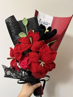 a person holding a bouquet of red flowers in their hand with black lace on it