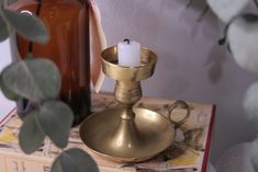 a brass candle holder on top of a book next to a bottle and eucalyptus leaves