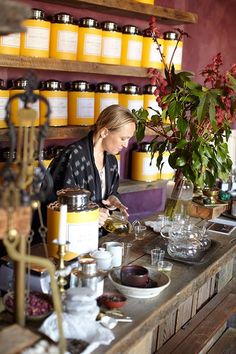 a woman sitting at a counter in front of some jars and containers filled with flowers