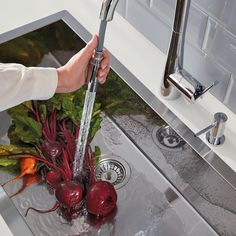 a person washing radishes in a sink with water running from the faucet