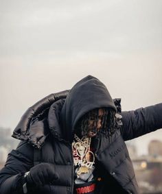 a man with dreadlocks and a jacket on holding his hands out to the side