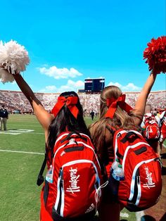 two cheerleaders in red and white outfits on the sidelines at a football game