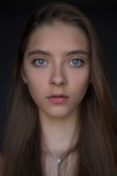 a woman with long brown hair and blue eyes is looking at the camera while wearing a necklace