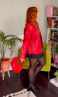 a woman with red hair is standing in front of a green chair and bookshelf