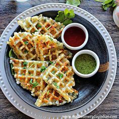 some waffles are on a plate with dipping sauce and green stuff next to them