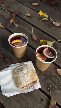 two cups of tea and a pastry on a wooden table with autumn leaves around them