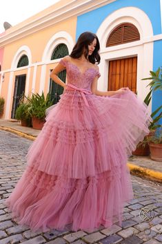 a woman in a pink dress standing on a cobblestone street with her hands behind her back