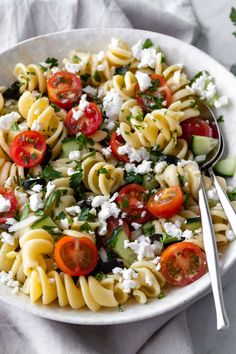 a white bowl filled with pasta salad and topped with fettuccine, tomatoes, cucumbers, and parsley