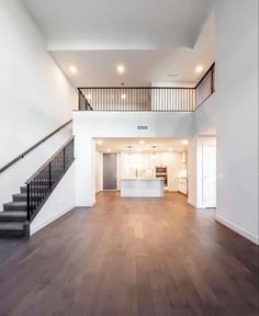 an empty living room with stairs leading up to the second floor and kitchen in the background