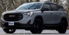 the front end of a gray gmc suv driving on a snowy road with trees in the background