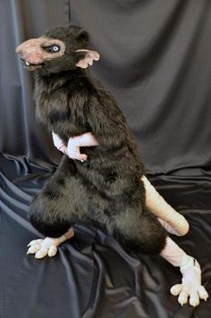 a stuffed animal rat sitting on top of a black cloth covered surface with its legs spread out