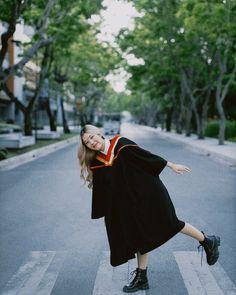 a woman in graduation gown crossing the street with her arms out and legs spread wide