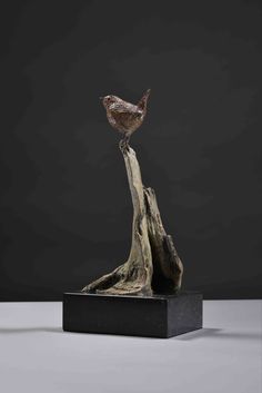 a sculpture of a bird sitting on top of a piece of driftwood in front of a black background