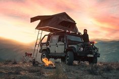 a man sitting on top of a truck next to a campfire in the desert