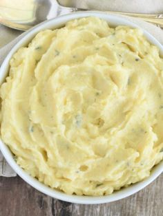 a white bowl filled with mashed potatoes on top of a wooden table next to silverware