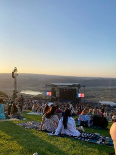 a group of people sitting on top of a lush green field next to a stage