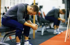 a man sitting on top of a bench in a gym holding his hands to his knees