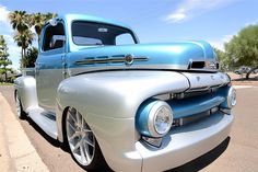 an old blue and silver truck parked on the side of the road with palm trees in the background