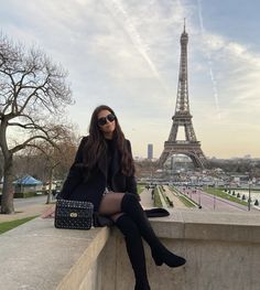 a woman sitting on top of a wall next to the eiffel tower